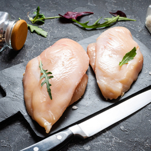 Two chicken breasts on a black cutting boards with a knife